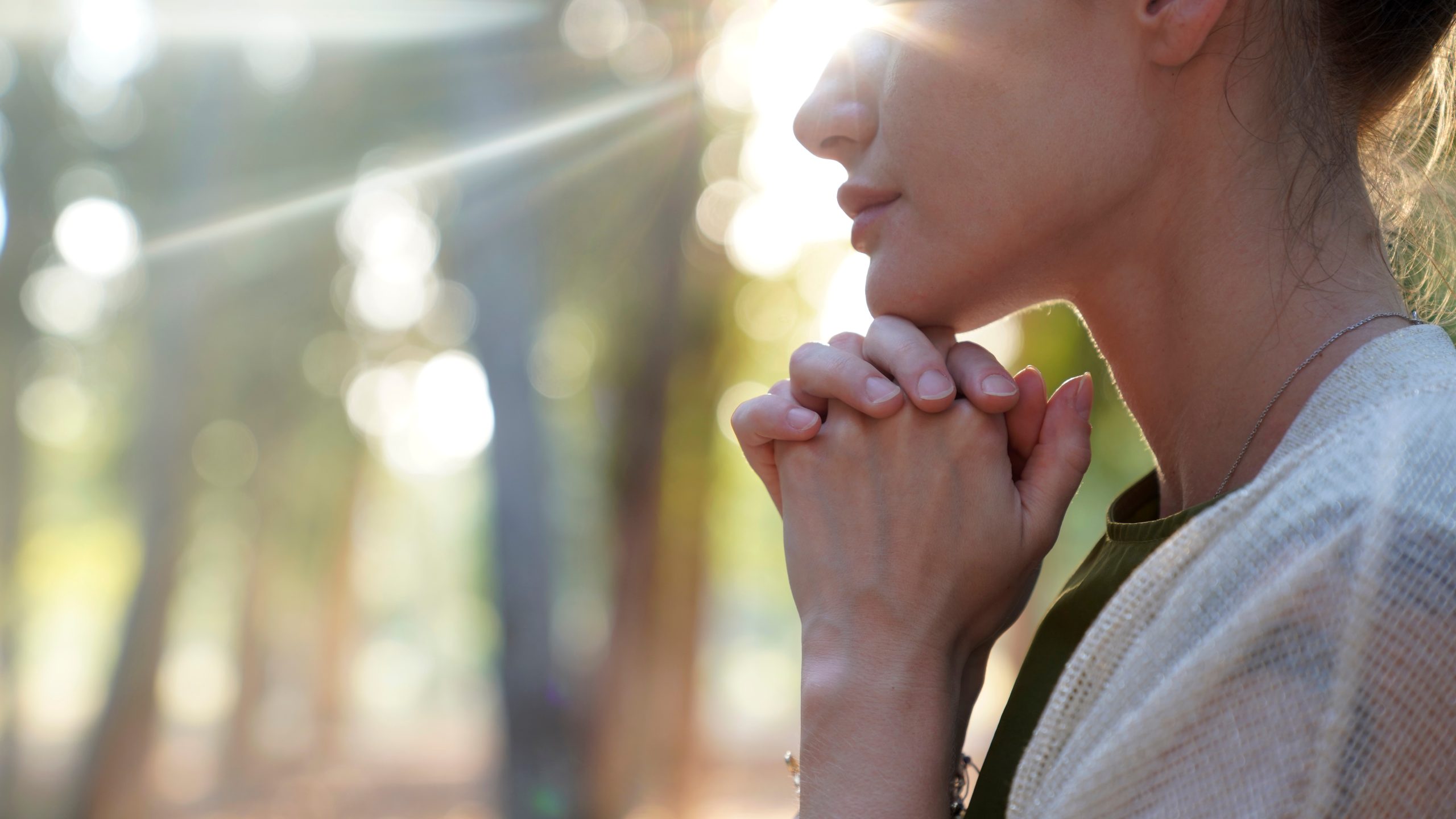 A woman with her eyes closed in the light through the trees