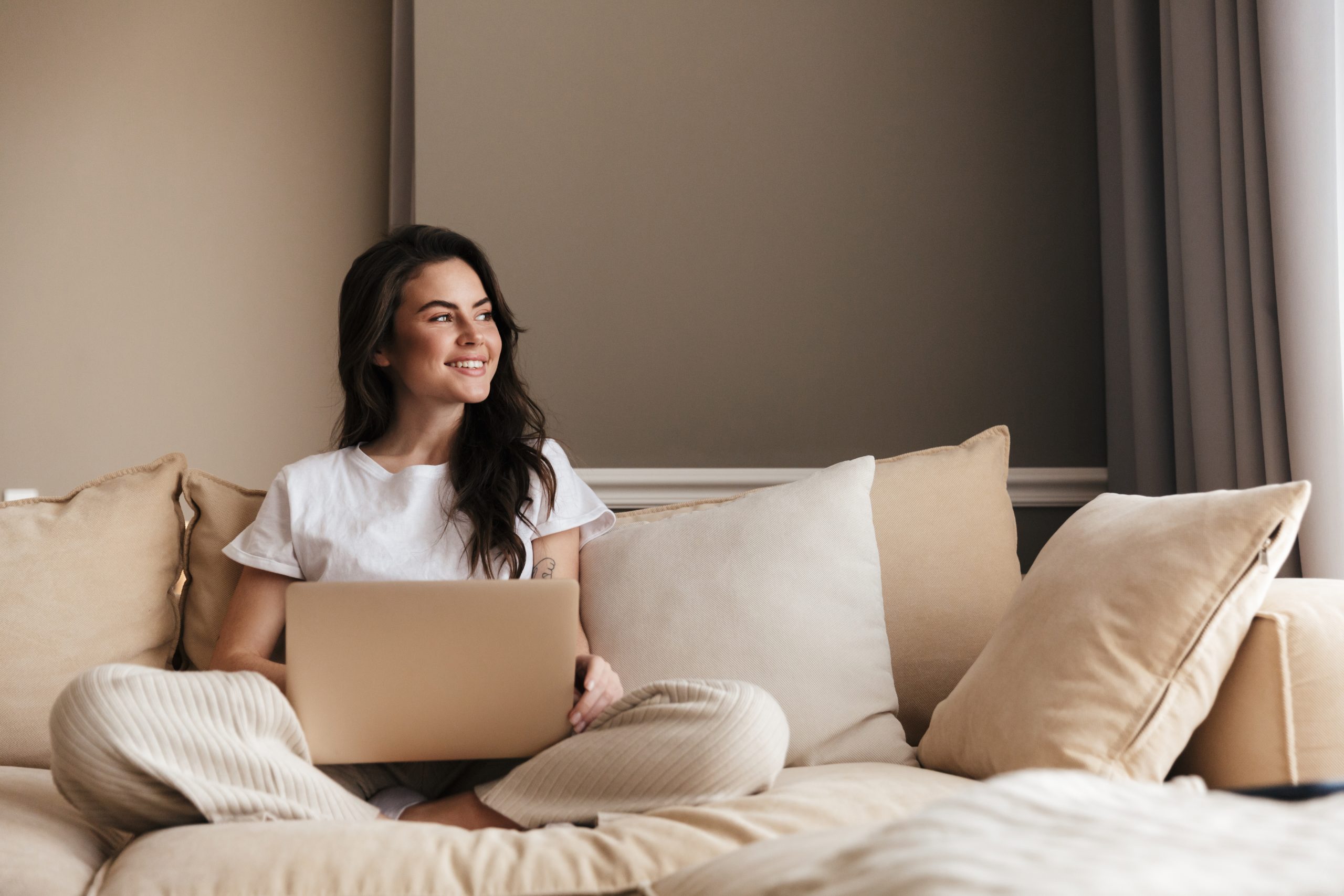 A woman sitting on her couch with a laptop